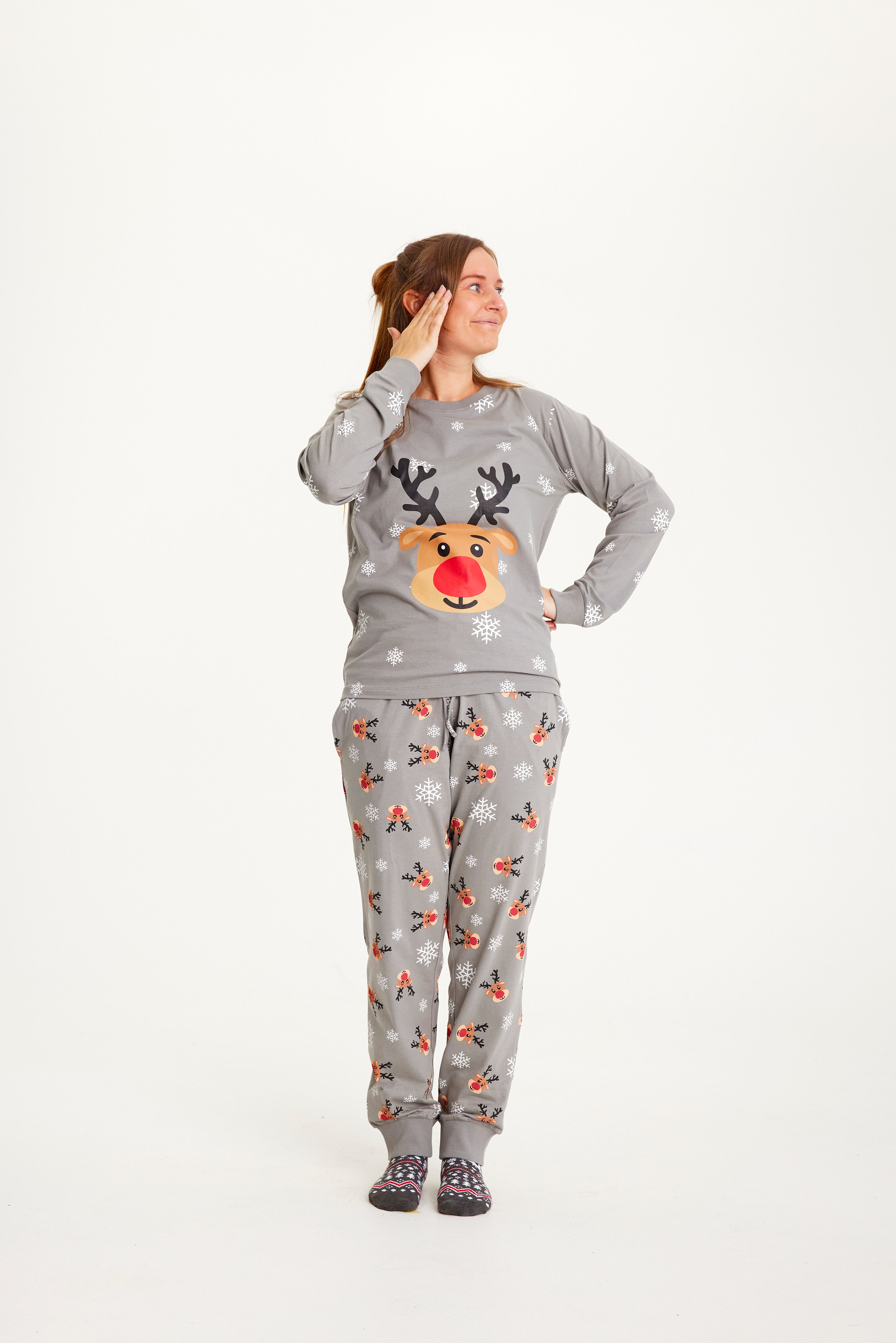 En kvinne i grå julepyjamas med reinsdyr og snøfnugg.